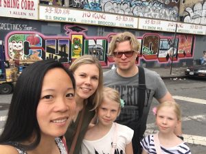 Jenni H. and family from Finland pause for a group photo with Greeter Diane in front of the Chinatown mural (New York City)